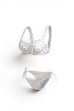 Bộ bikini Women in Lov3 màu trắng họa tiết hoa nhỏ, áo có gọng, bèo nhún và quần dây buộc bên hông.